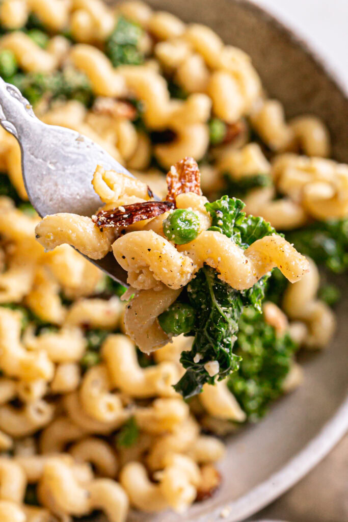 a close up of some garlicky kale pasta on the fork with the bowl out of focus in the background