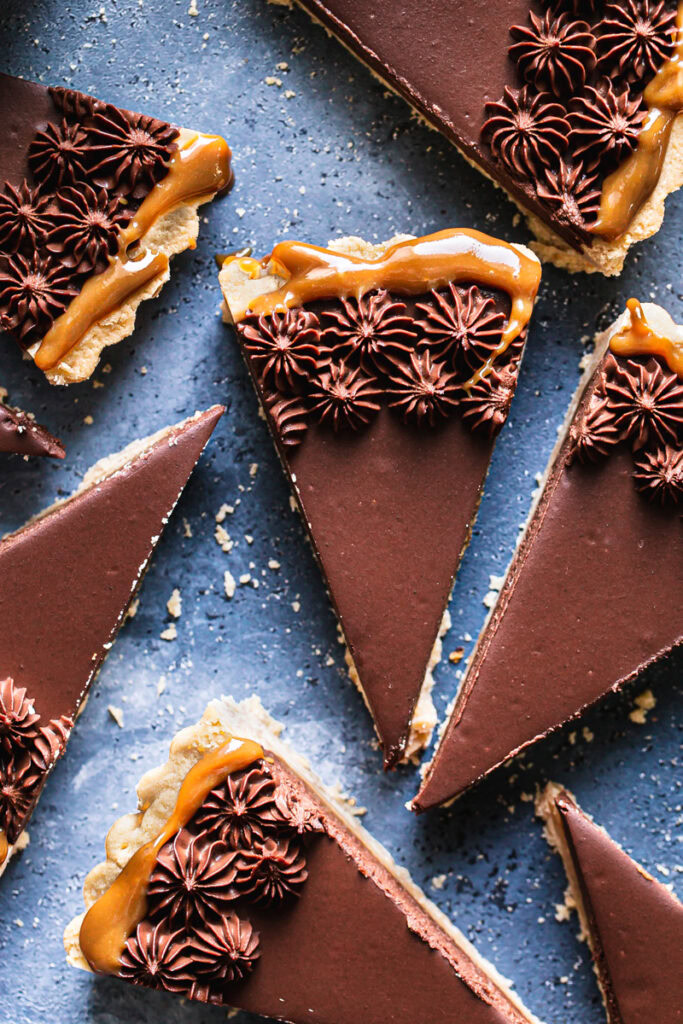 a close up of slices of Twix tart piped with chocolate mousse on a blue backdrop