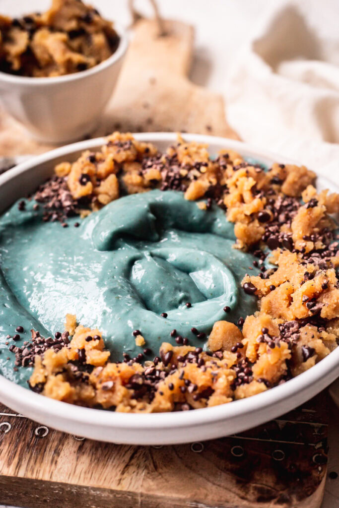 a side view of a blue spirulina smoothie bowl topped with almond flour cookie dough sprinkled with chocolate covered chia seeds