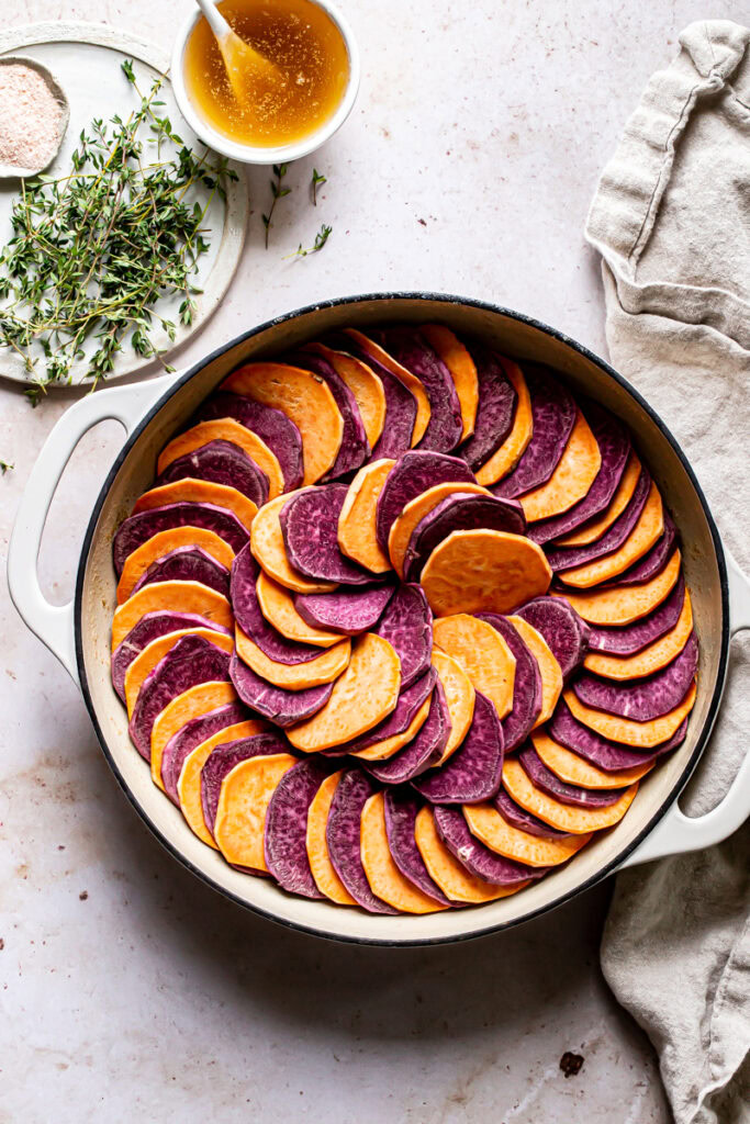 a prep image of the uncooked sweet potatoes alternating in color in a swirl pattern with a plate of thyme and salt on the side, a linen napkin and a bowl of browned butter with a spoon
