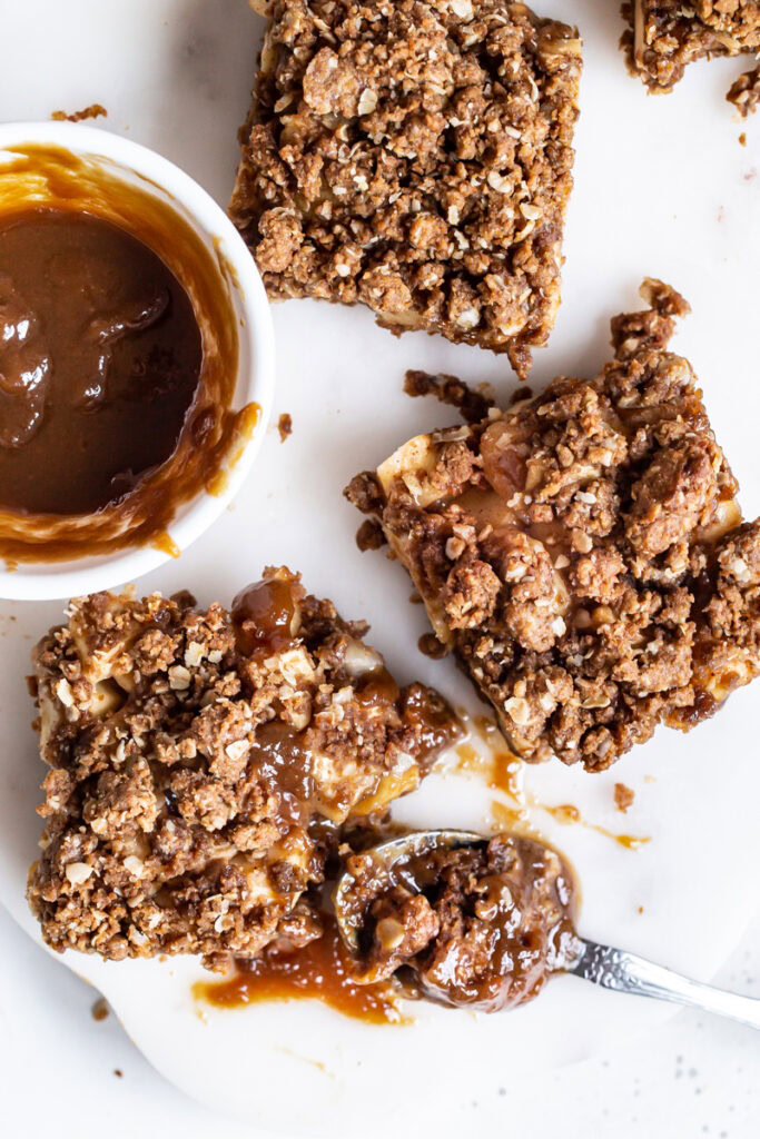 caramel apple crumb bars flatly with a bowl of caramel sauce and a spoonful of crumb bar with caramel