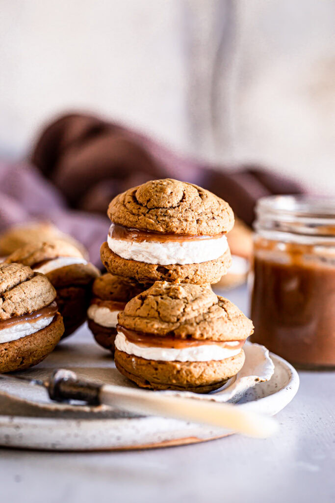 apple butter whoopie pies stacked on top of each other with a jar of apple butter in the background
