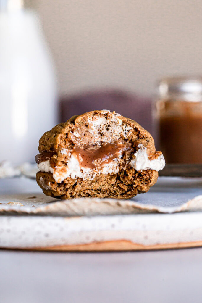 up close bite shot of an apple butter whoopie pie on a plate with a jug of milk and jar of apple butter blurred in the background