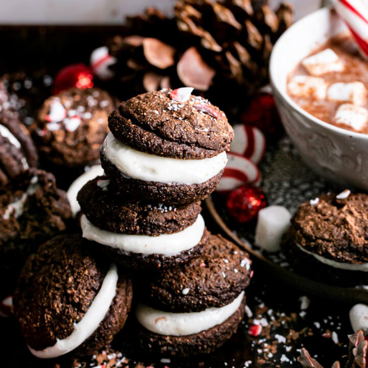 three hot cocoa whoopie pies stacked on top of one another with a cup of hot cocoa in the background