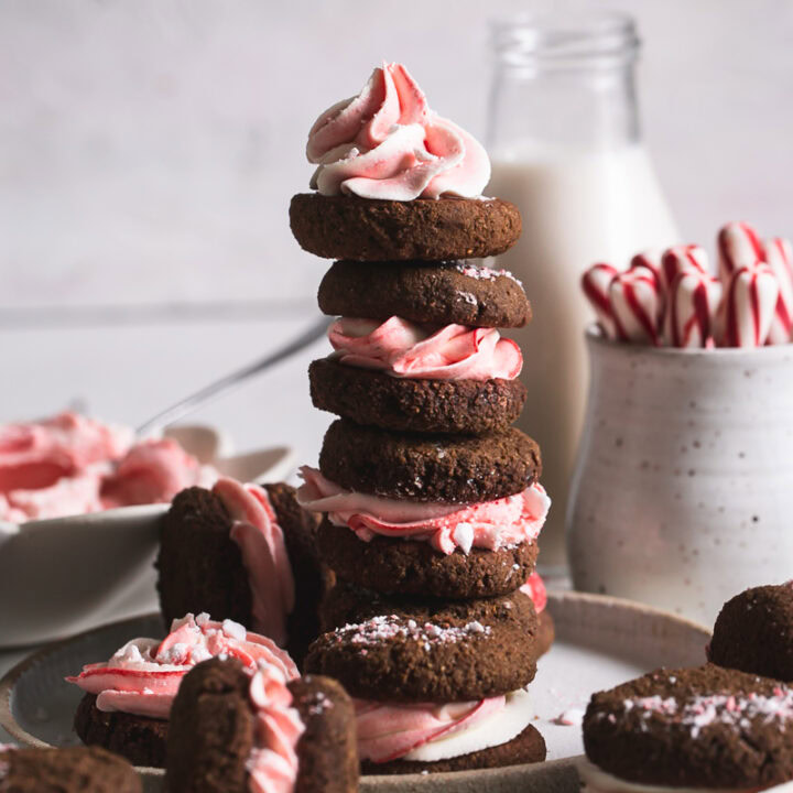 a stack of peppermint cream sandwich cookies with a jar of almond milk and candy cane sticks in the background