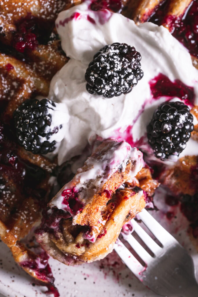 a close-up overhead shot of blackberry waffles with a bite of waffles on a fork