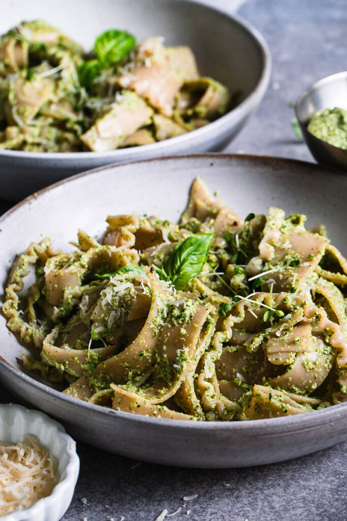 a side close up shot of a bowl of olive pesto pasta with another bowl blurred in the background