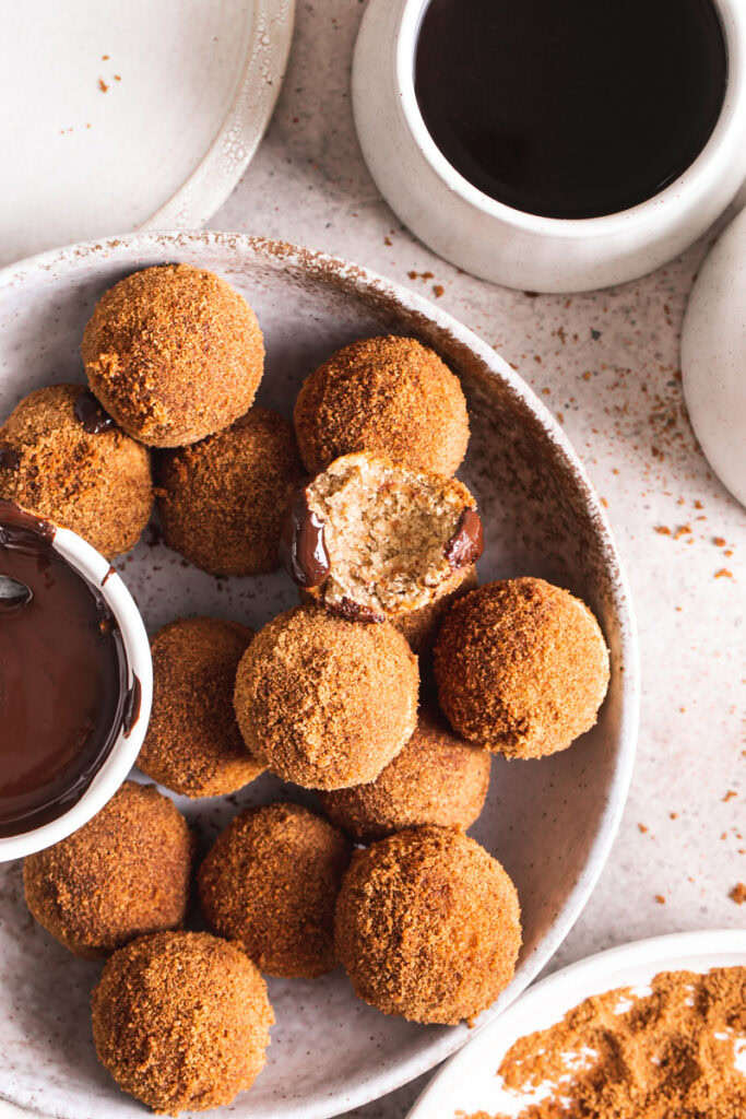 a side view of gluten-free, grain free, vegan, naturally sweetened churro donut holes with a bowl of melted chocolate for dipping and one of the donut holes with a bite taken out of it
