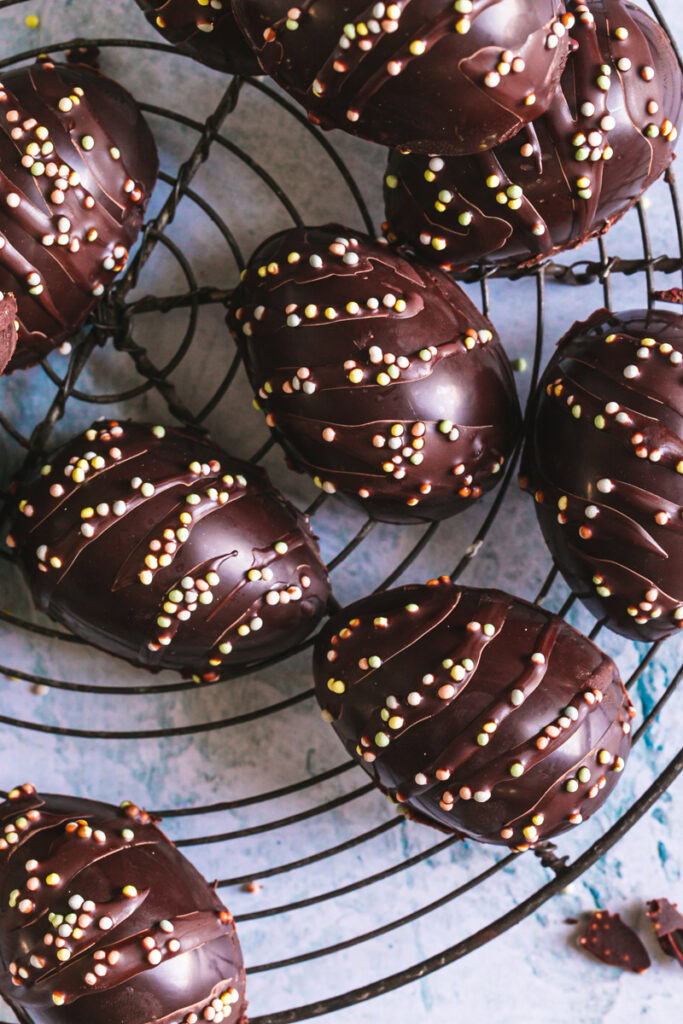 an overhead image of chocolate eggs decorated with sprinkles on a French round cooling wire rack