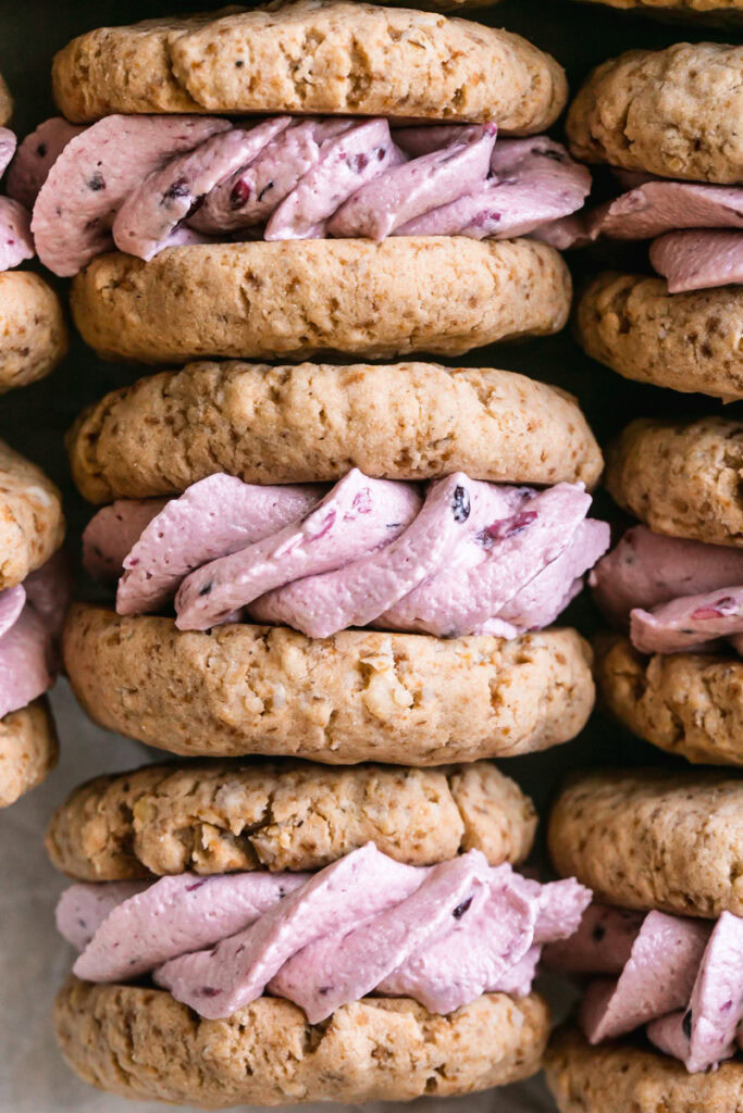 close up flat lay shot of oatmeal sandwich cookies with blackberry cream filling laid in a tray all lined up with the cream filling showing