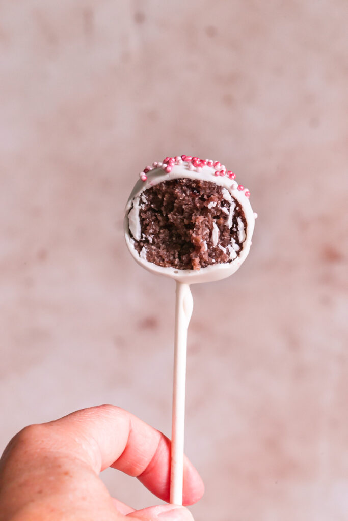 a single cherry cake pop with a bite taken out of it being held