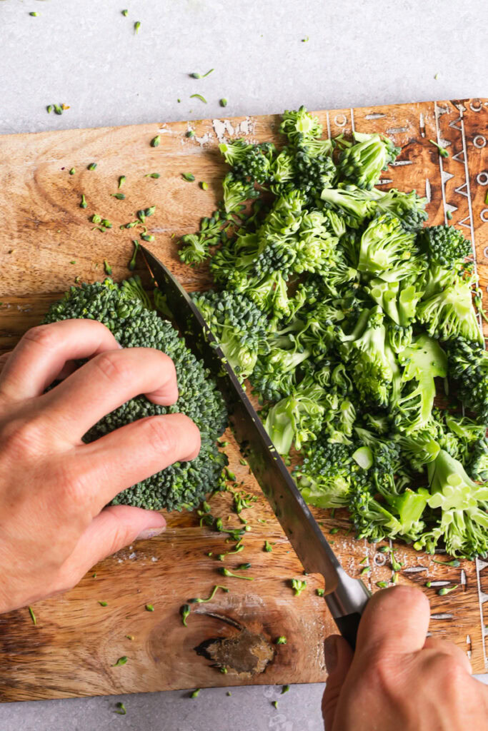 action shot of hands chopping broccoli on a cutting board