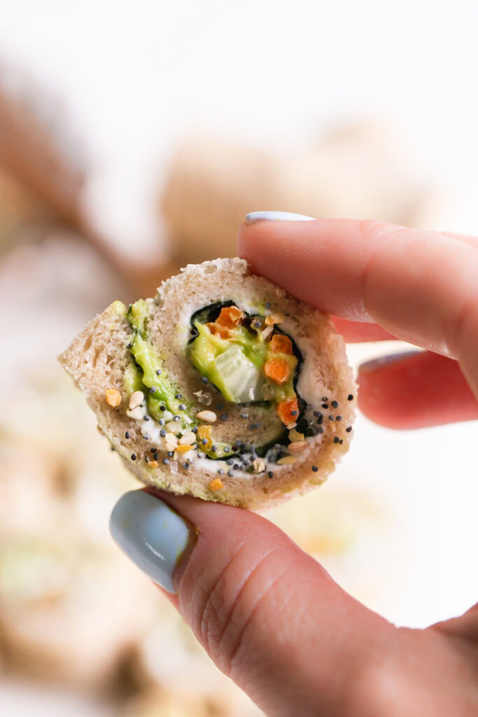 a single slice of veggie sushi sandwich rollup held in between fingers revealing the veggie filling