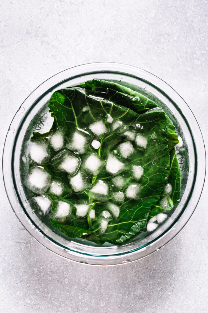 blanched collard wraps submerged in a bowl of ice water