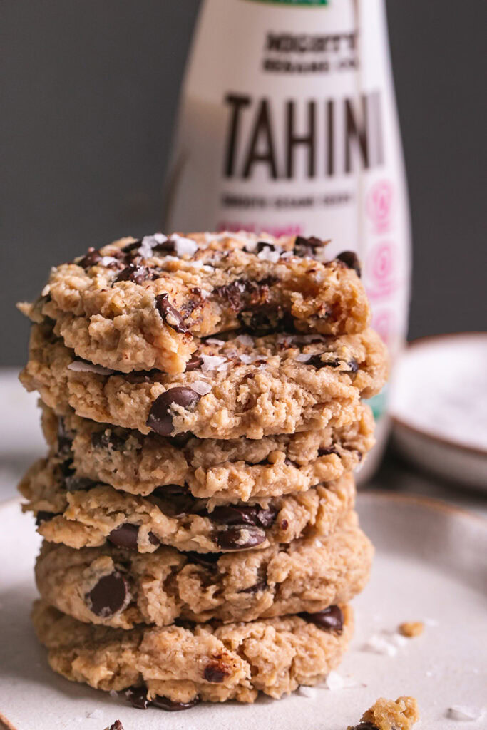 a stack of flourless salted tahini chocolate chip cookies and a bottle of mighty sesame co organic tahini in the background