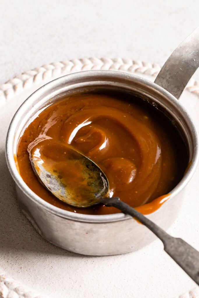 3/4 view of the caramel in a small saucepan with a spoon in it