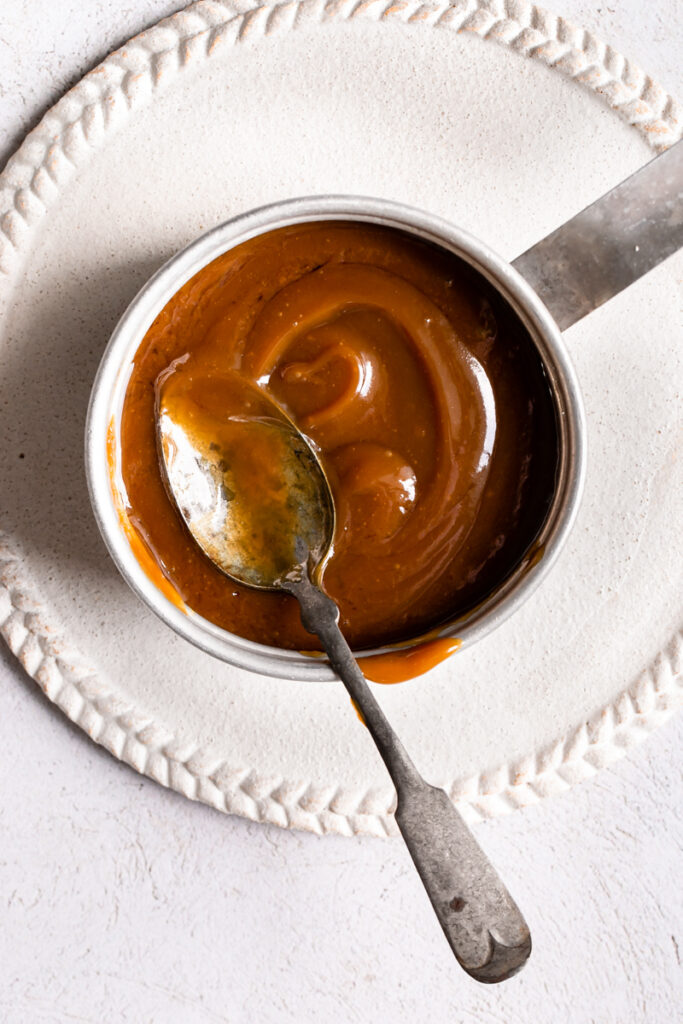 small saucepan with caramel in it on a plate with a spoon sticking out of it