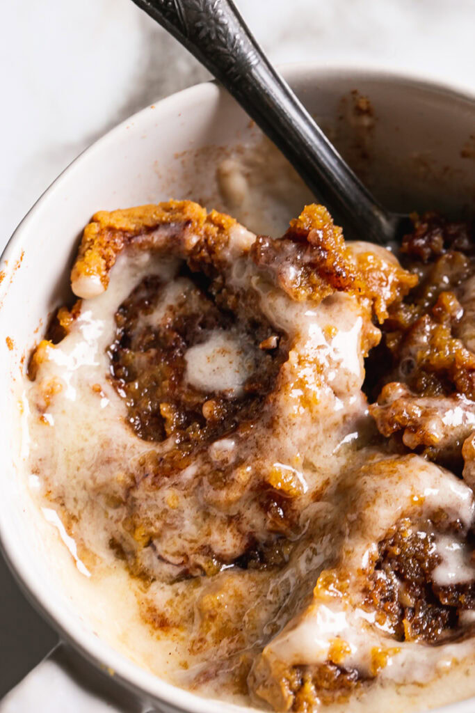 close up of the pumpkin cinnamon roll mug cake frosted with a spoon sticking out of the mug