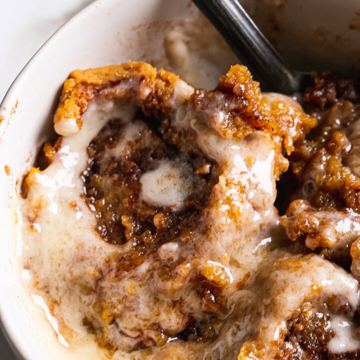 close up of the pumpkin cinnamon roll mug cake frosted with a spoon sticking out of the mug
