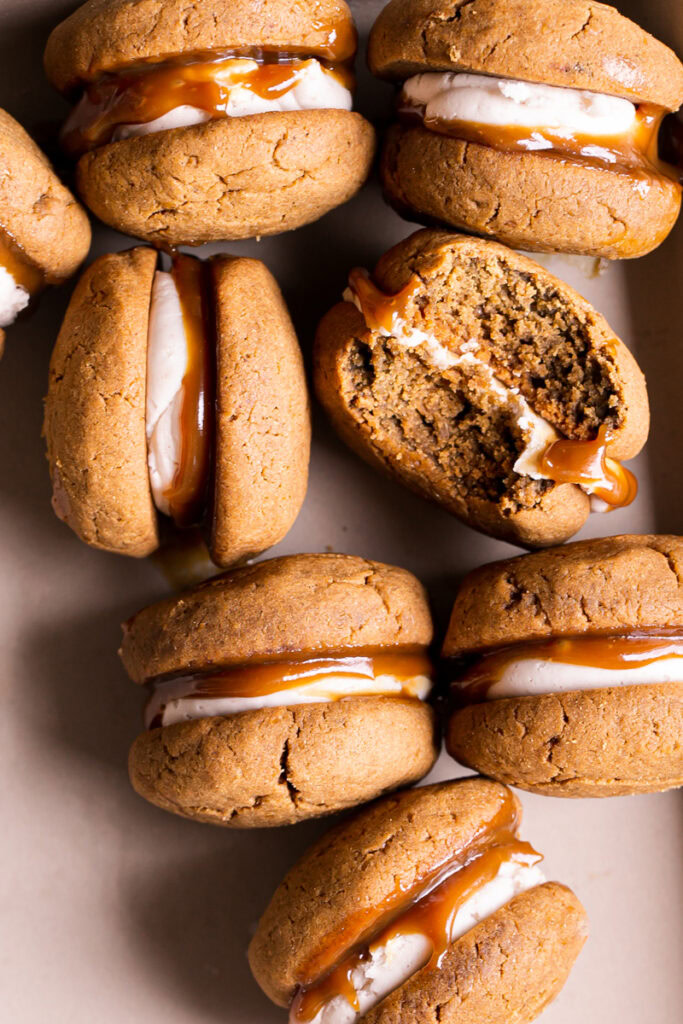 overhead shot of pumpkin spice latte whoopie pies revealing the buttercream and caramel filling, one with a bite taken out of it