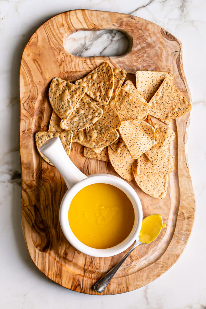 an overhead shot of a bowl of vegan nacho cheese sauce on a wooden cutting board with tortilla chips laid out with it