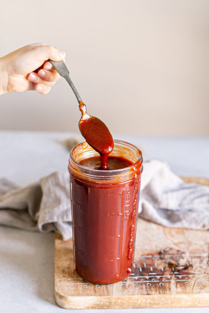 a jar of homemade Gluten-free Vegan Pumpkin BBQ Sauce with a spoon dripping some off into the jar