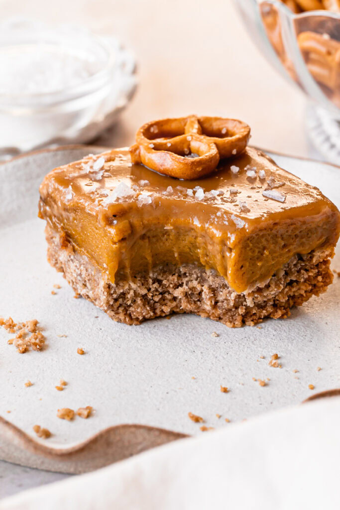 3/4 shot of Salted Caramel Pumpkin Pie Bars with Pretzel Crust on a plate with a bite taken out of it