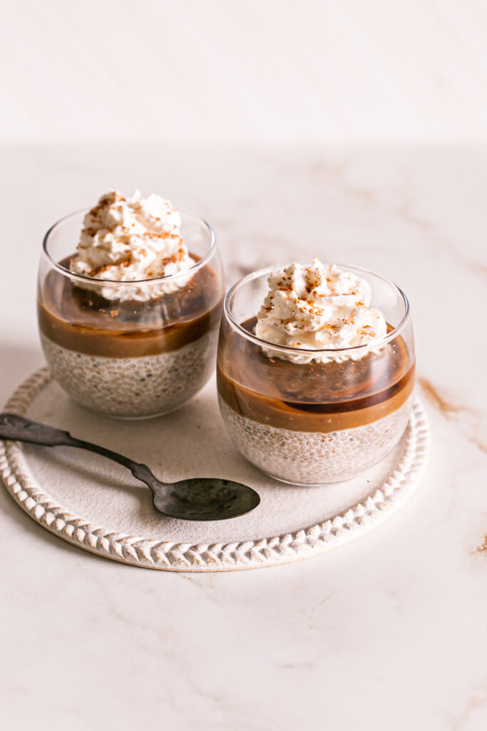 3/4 view of two glasses of caramel eggnog chia pudding topped with vegan caramel, maple syrup and whipped cream