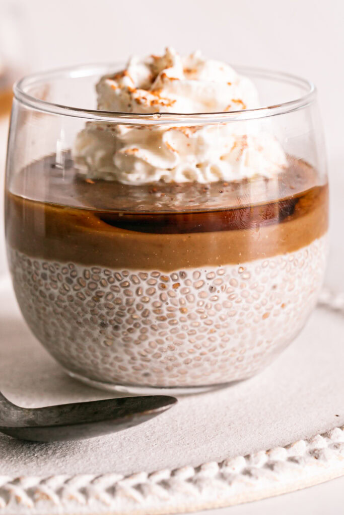 a close up shot of a glass of caramel eggnog chia pudding topped with vegan caramel, maple syrup and whipped cream