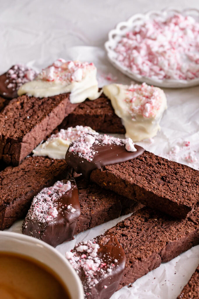 3/4 close up shot of Gluten-Free Chocolate Peppermint Biscotti with a plate of crushed peppermints in the background