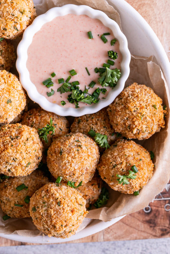 close up image of a bowl full of mashed potato croquettes with a bowl of paprika dipping sauce garnished with fresh chives and parsley