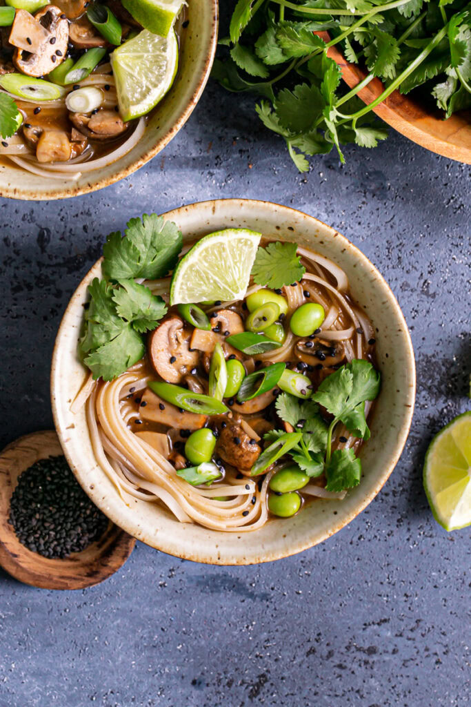 a close up of one of the bowls of mushroom pho with another bowl peeking in the corner and the bowl of fresh cilantro peeking in the other corner