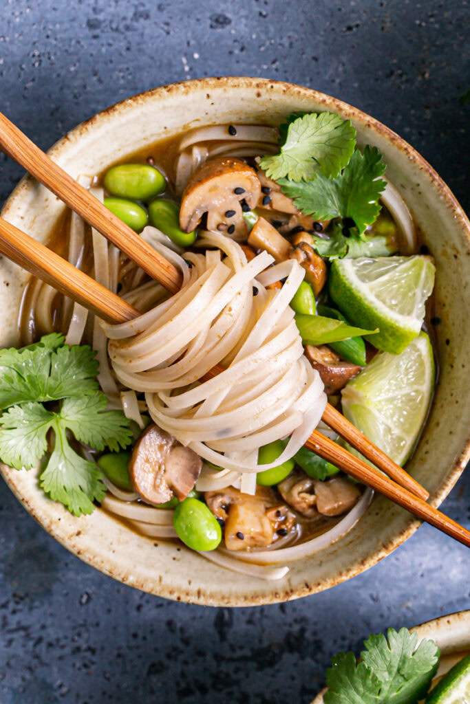 a close up of a bowl of mushroom pho with noodles wrapped around chopsticks