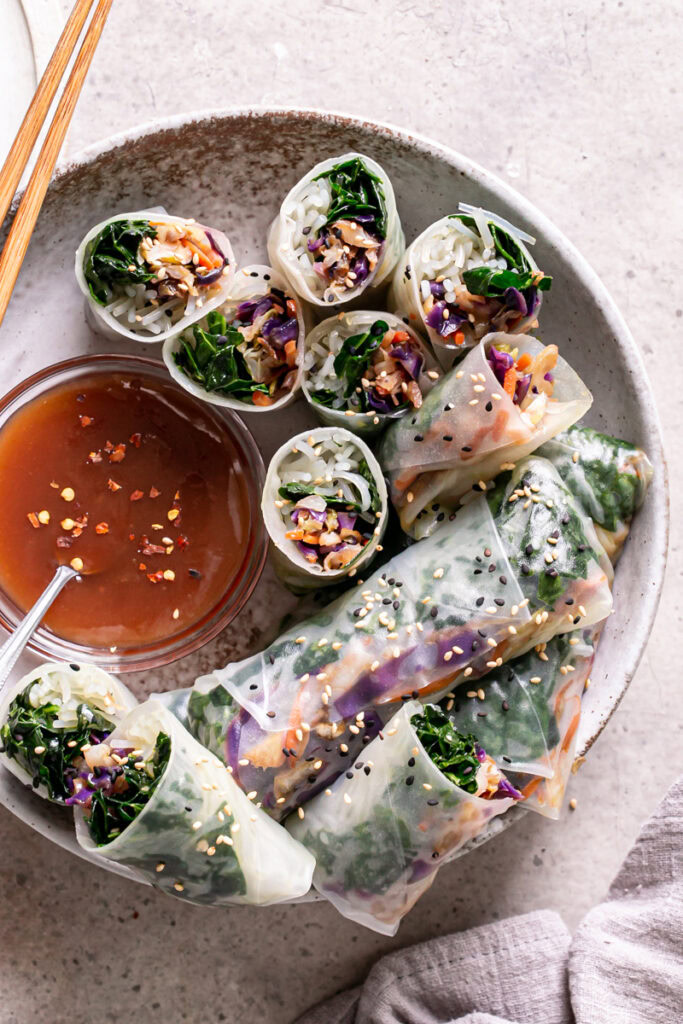 sesame kale spring rolls in a bowl, some cut in half to reveal the filling, served with a bowl of sweet and sour sauce