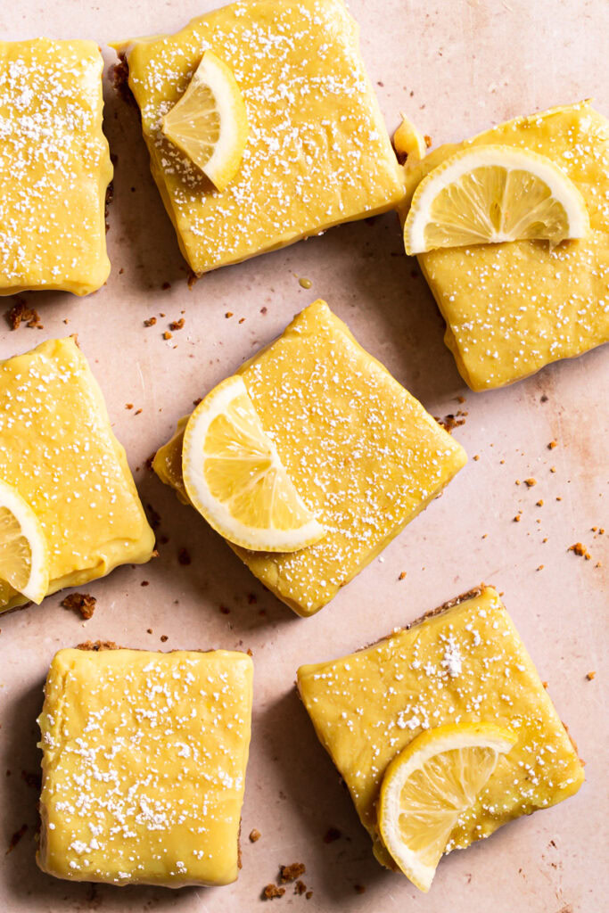 overhead photo of lemon bars cut up into squares and separated dusted with powdered sugar and fresh lemon slices
