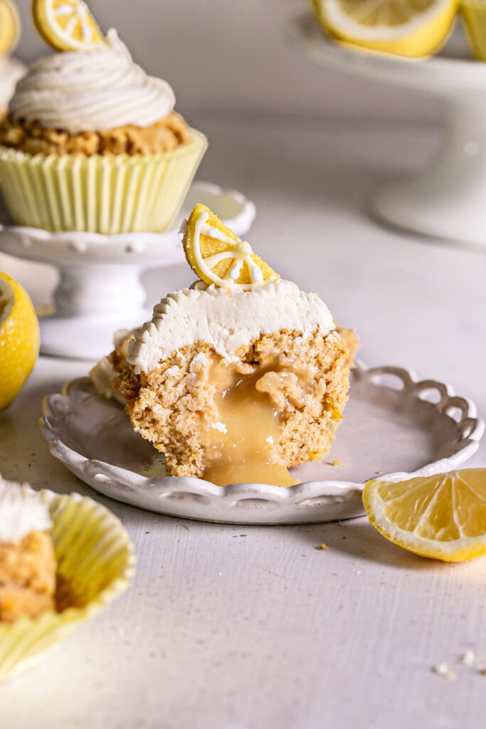 grain-free lemon cupcake cut in half to show the lemon curd filling with other cupcakes and lemon wedges around it