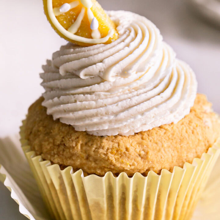 a close up of a frosted grain-free lemon cupcake with a candy lemon wedge on top