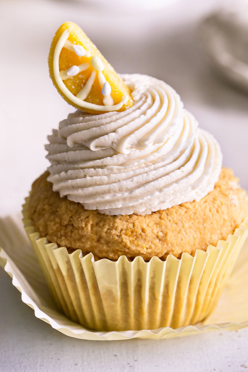 a close up of a frosted grain-free lemon cupcake with a candy lemon wedge on top