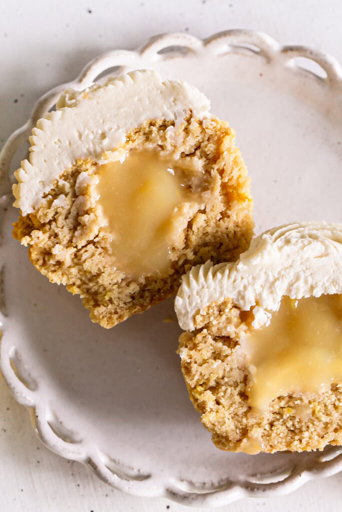 flatlay image of a frosted grain-free lemon cupcake cut in half to reveal the lemon curd filling