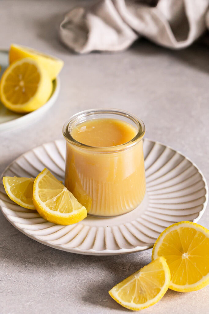 a jar of lemon curd on a plate with fresh lemons around it