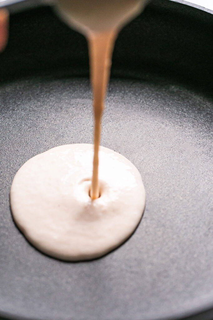 action shot of pouring the gluten-free vegan crepe batter into the calphalon fry pan