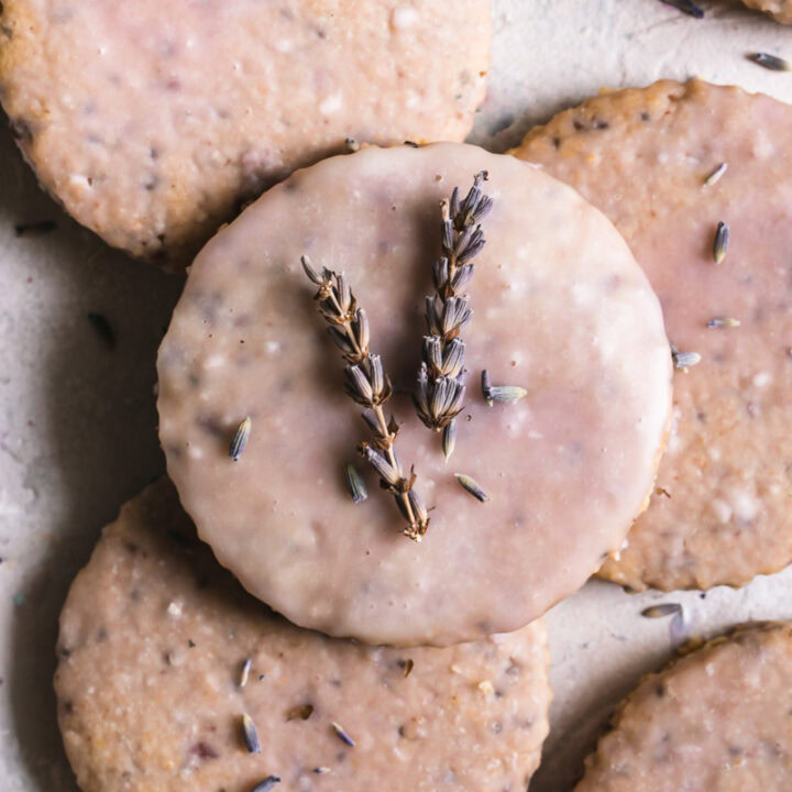 Lavender Vanilla Oatmeal Shortbread Cookies piled on top of one another iced with a light purple icing, the top cookie with lavender sprigs on top
