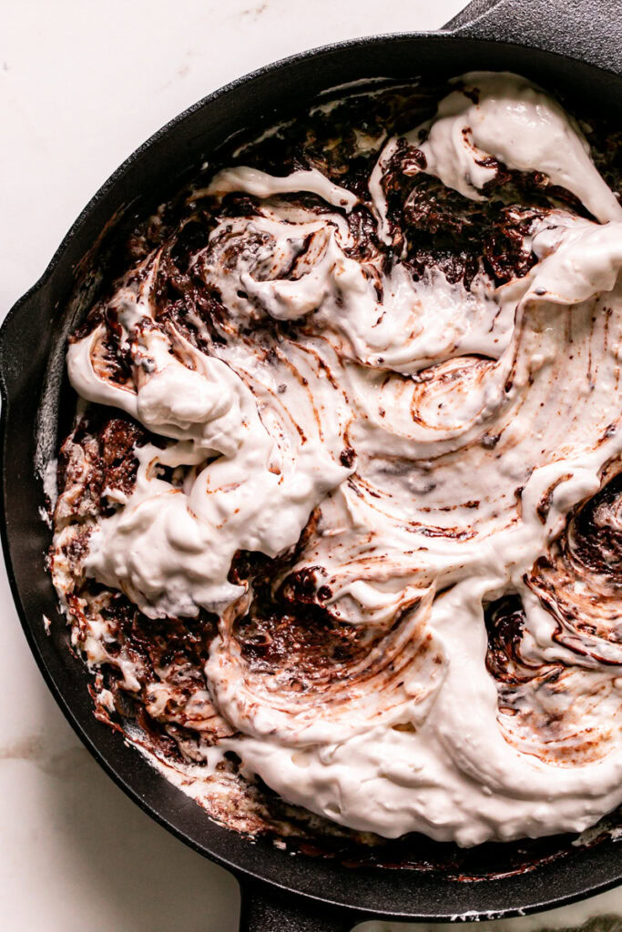 close up shot of untoasted marshmallow fluff swirled with the melted chocolate in the cast iron skillet