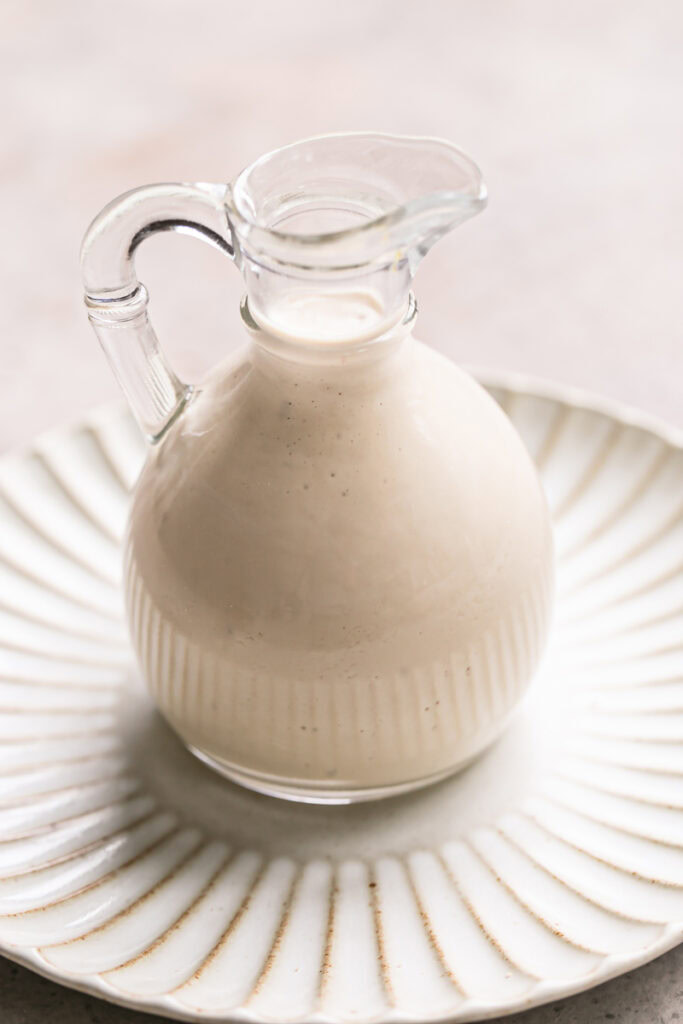 close up image of creamy tahini dressing in a glass oil bottle on a plate