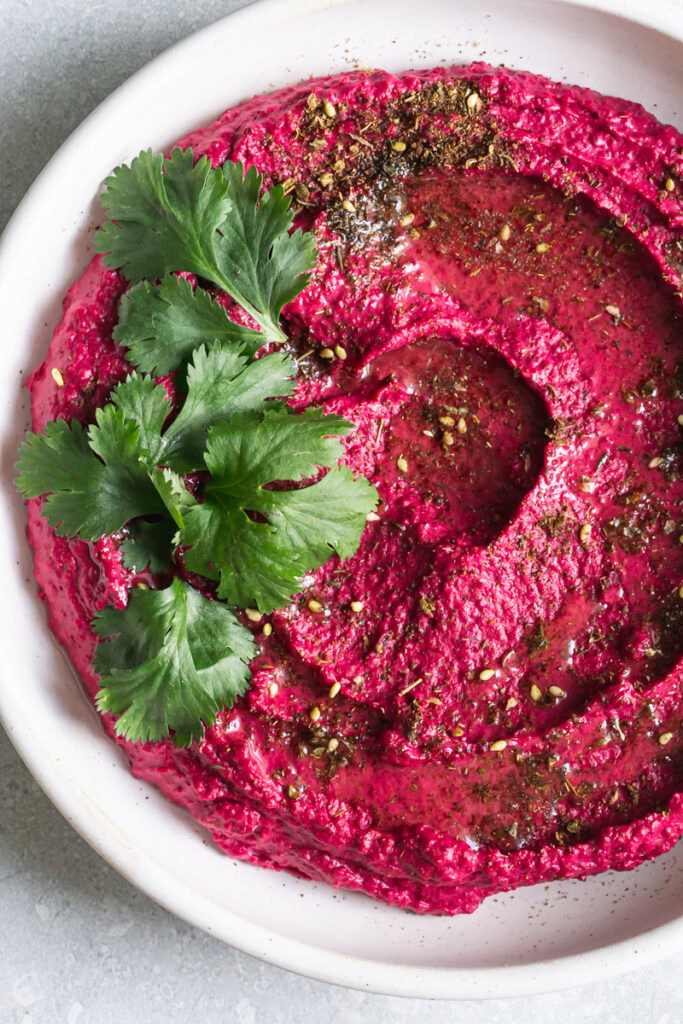 close up of a bowl of Za'atar Roasted Beet White Bean Hummus garnished with fresh cilantro leaves