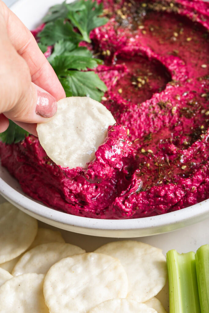 action shot of dipping a rice cracker in the roasted beet hummus