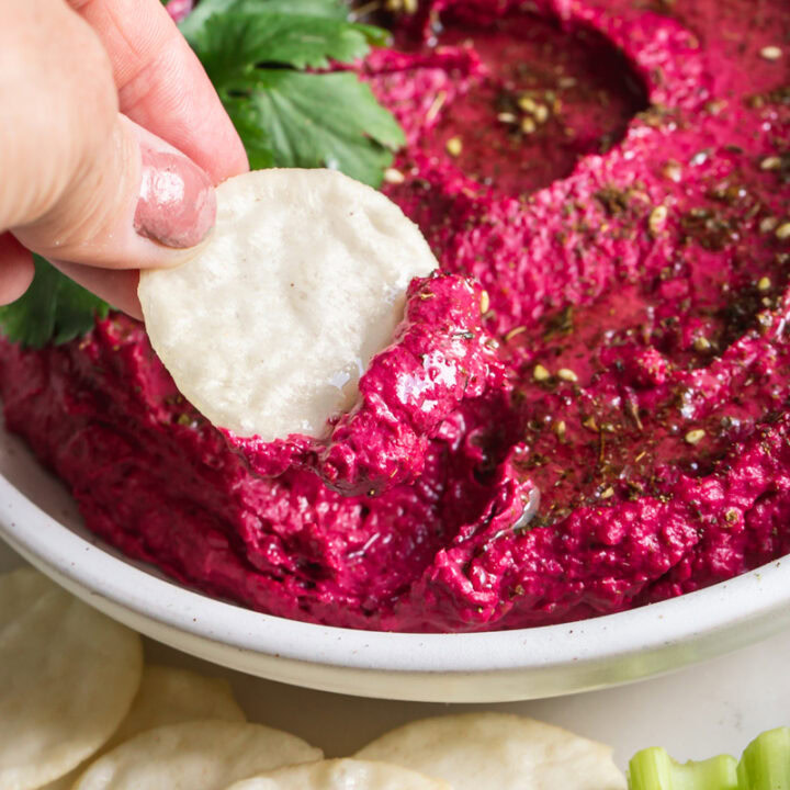 action shot of dipping a rice cracker in the roasted beet hummus