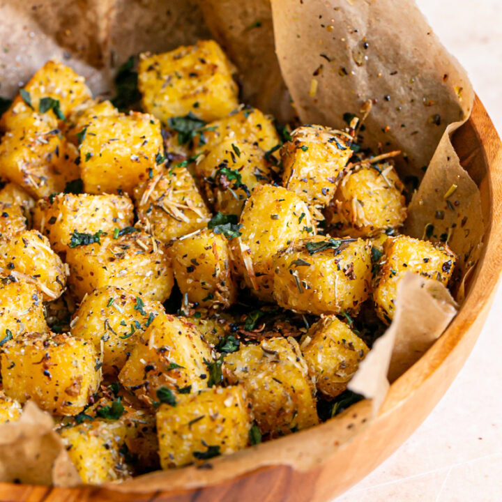 3/4 close up of polenta croutons in a wooden bowl lined with parchment paper