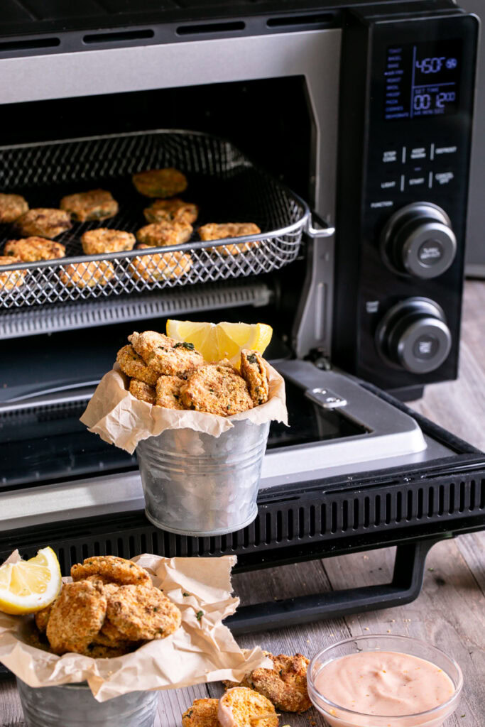 gluten-free air fryer fried pickles in front of an open calphalon air fry oven with fried pickles in the air fryer basket