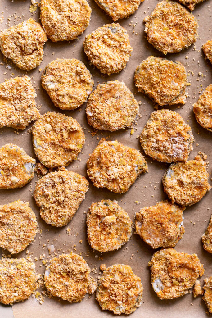 un-fried pickle slices on a baking sheet coated in gluten-free breading